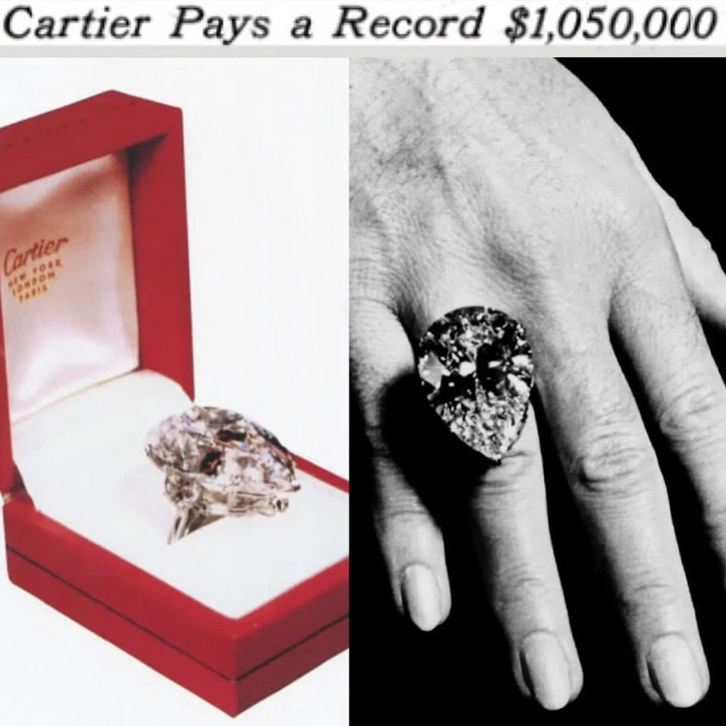 Large pear-shaped diamond ring in a red Cartier box and worn on a hand.